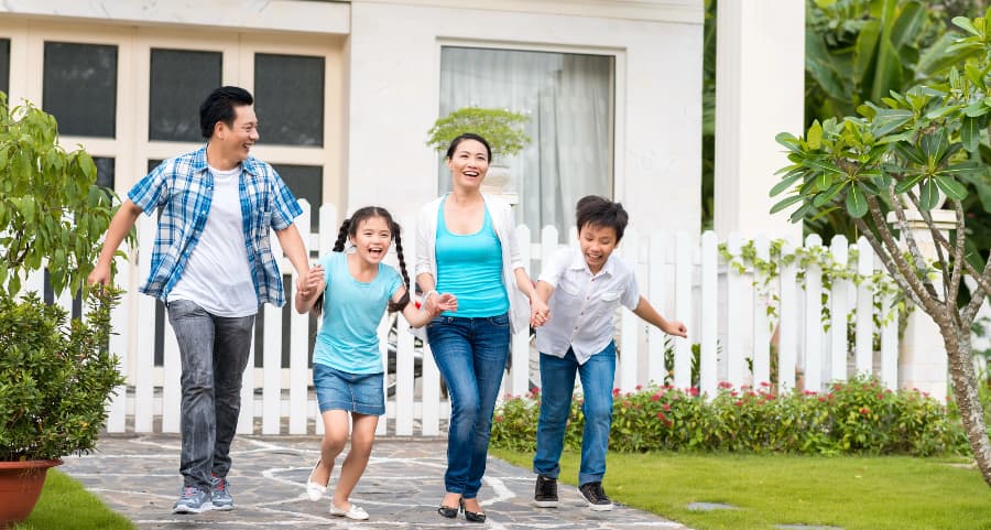 Parents and kids walking together in front of a beautiful home with white fencing